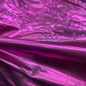 May include: Close-up of a deep purple iridescent fabric with a smooth, silky texture. The fabric is folded and draped, showcasing its shimmering quality.