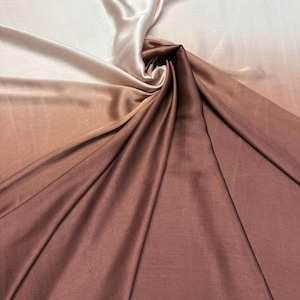 May include: A luxurious fabric with a color gradient, transitioning from off-white to a rich brown. The material is smooth and appears to be silk or satin, with soft folds and a subtle sheen. Ideal for apparel or home decor.