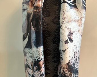 Puede incluir: Una bufanda drapeada con un diseño artístico único. La bufanda presenta una mezcla de colores que incluyen negro, blanco y tonos de azul y melocotón. El diseño incorpora elementos florales y abstractos, con patrones tipo texto.