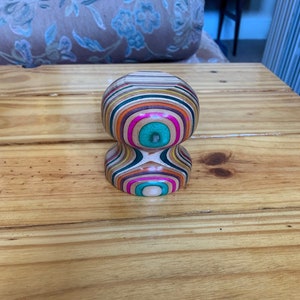 May include: A colourful wooden knob with a layered pattern of pink, green, brown, and orange. The knob is round and has a smooth surface.
