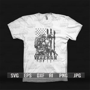May include: A white t-shirt with a black and white graphic of a soldier standing in front of an American flag. The text "VETERAN" is printed below the soldier.