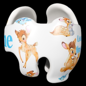 Puede incluir: Artículo decorativo de cerámica blanca con ilustraciones de Bambi y otros personajes. El artículo tiene una forma única con recortes y las palabras "Love that" en azul. También aparece un pájaro azul.