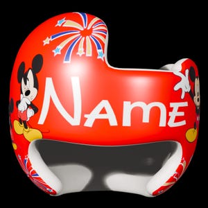 Könnte beinhalten: Ein leuchtend roter Kopf-Korrekturhelm mit einem sich wiederholenden Muster aus Mickey-Mouse-Figuren und bunten Feuerwerksdarstellungen. Das Wort NAME ist in großen weißen Großbuchstaben auf dem vorderen Mittelteil aufgedruckt.