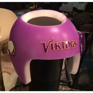 Könnte beinhalten: Lilafarbener Helm mit weißem Rand und weißem Riemen. Der Helm hat ein lilafarbenes und goldenes "Vikings"-Logo auf der Vorderseite.