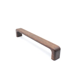 Może przedstawiać: Rektangularny, ciemnobrązowy, zaokrąglony uchwyt do szafki wykonany z drewna.