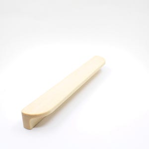 Può includere: Una maniglia per mobili in legno di colore chiaro. La maniglia ha una forma rettangolare con bordi arrotondati e un design curvo. La maniglia è in legno, probabilmente per un cassetto o un'anta dell'armadio.