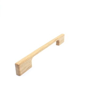 Puede incluir: Un tirador de armario de madera de color marrón claro, de forma rectangular con un hueco para el agarre.