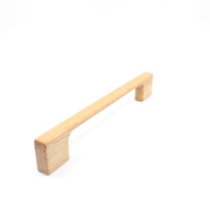 Può includere: Una maniglia per armadio in legno di colore marrone chiaro, di forma rettangolare con un manico leggermente curvo.