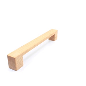 May include: A light brown wooden cabinet pull with a rectangular shape.