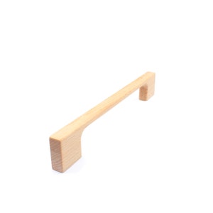Könnte beinhalten: Ein heller Holz-Schrankgriff mit rechteckiger Form und einer leichten Biegung in der Mitte.