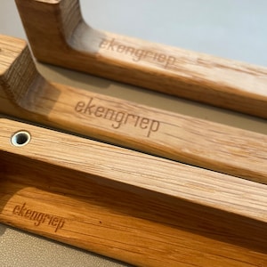 Könnte beinhalten: Nahaufnahme von drei Holzgriffen mit gebogenem Design. Jeder Griff besteht aus hellem Holz und trägt das eingravierte Wort "ekengriep". Die Griffe haben eine rechteckige Basis mit einer Metallschraube.