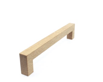 May include: A light brown wooden cabinet pull with a rectangular shape. The pull has a simple design with a slight curve on the top.