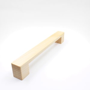 Könnte beinhalten: Ein rechteckiger, heller Holzknauf für Schränke. Der Knauf ist etwa 15 cm lang.