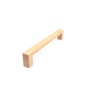 Puede incluir: Un tirador de armario de madera de color marrón claro con forma rectangular.