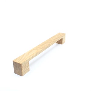 Può includere: Una maniglia per armadio in legno di colore marrone chiaro con forma rettangolare.