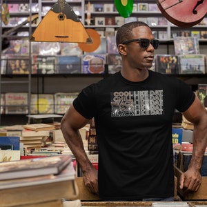 May include: A black t-shirt with a white graphic print that reads "COOL LIKE DAT, CHILL LIKE DAT, PEACE LIKE DAT, JAZZ LIKE DAT, BLACK LIKE DAT".