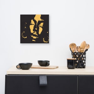 May include: A black and gold canvas print featuring a stylized portrait of a person with their eyes closed. The portrait is in a minimalist style with a focus on the face.