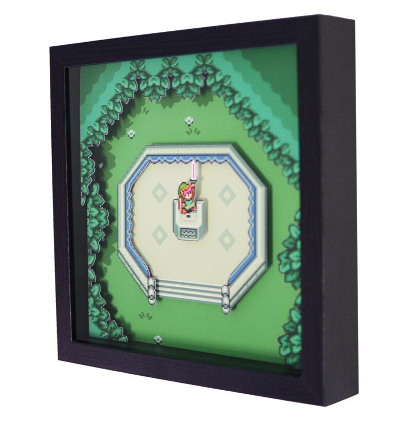 May include: A framed 3D art piece featuring a pixelated scene from a video game. The artwork depicts a character holding a glowing sword in a green landscape with a white and blue structure. The frame is black.