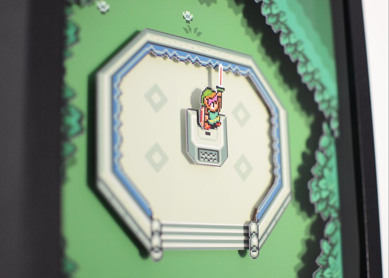 May include: A framed pixel art piece featuring a scene from a video game. The artwork depicts a character with a sword in a white and blue octagonal structure, set against a green background with pixelated foliage. The piece is framed in black.
