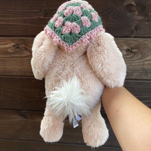 May include: A pink plush bunny with a white fluffy tail wearing a green and pink crocheted hat.