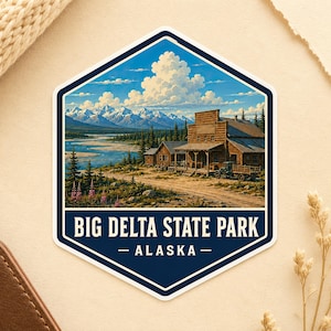 May include: A hexagonal sticker featuring a landscape illustration of Big Delta State Park in Alaska. The scene depicts a rustic wooden building, a vintage truck, a winding river, and snow-capped mountains under a blue sky with white clouds.