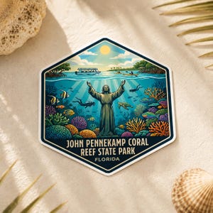 Op de afbeelding: Een zeshoekige sticker met een onderwaterlandschap met een standbeeld, koraal, vissen en duikers. De tekst "JOHN PENNEKAMP CORAL REEF STATE PARK FLORIDA" wordt weergegeven. De sticker heeft een witte rand en een blauwe achtergrond.