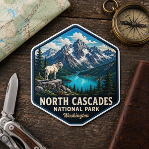 May include: A hexagonal sticker featuring a mountain goat standing on a rocky ledge overlooking a blue lake and snow-capped mountains. The text reads NORTH CASCADES NATIONAL PARK Washington in white and yellow lettering against a dark blue background.