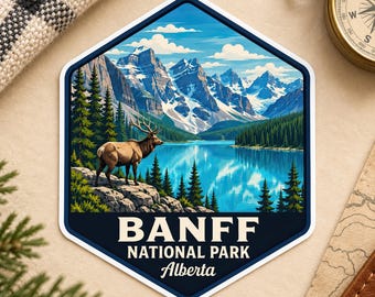 May include: A hexagonal sticker featuring a landscape illustration of Banff National Park in Alberta. The image displays a brown elk standing on a rocky shore overlooking a bright blue lake, surrounded by pine trees and snow-capped mountains.