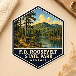 May include: A hexagonal sticker featuring a landscape illustration of F.D. Roosevelt State Park in Georgia. The scene depicts a calm lake surrounded by dense pine forests and rolling mountains under a blue sky with clouds. The text reads F.D. ROOSEVELT STATE PARK GEORGIA.