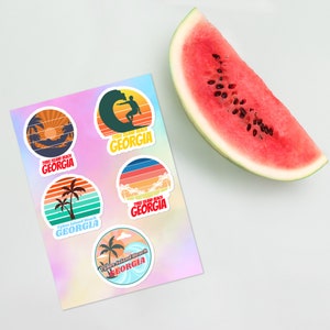 May include: A sheet of five colorful stickers with a retro design featuring the text "Tybee Island Beach Georgia". Each sticker has a different design, including a palm tree, a surfer, and a sunset.