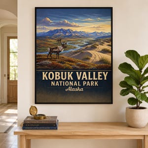 May include: A framed wall art print featuring a landscape illustration of Kobuk Valley National Park in Alaska, showing a caribou, a winding river, and mountains under a sunset sky, with the text KOBUK VALLEY NATIONAL PARK Alaska printed below.