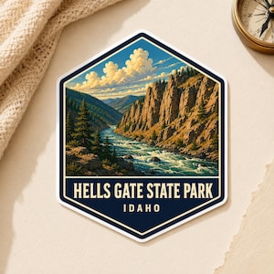 May include: A hexagonal sticker featuring a landscape illustration of Hells Gate State Park, Idaho. The image depicts a river flowing through a rocky canyon with pine trees under a blue sky with white clouds. The text reads HELLS GATE STATE PARK IDAHO.