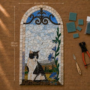 Può includere: Un mosaico da parete ad arco che misura 46 cm di larghezza per 88 cm di altezza, raffigurante un gatto bianco e nero, fiori blu e un paesaggio. Include tessere verdi sciolte, una piccola spatola e una tronchese per mosaico con manici arancioni.