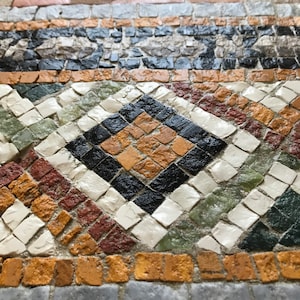 Könnte beinhalten: Nahaufnahme eines Mosaikfliesen-Designs mit einem Rautenmuster. Das Mosaik verwendet schwarze, braune, weiße, grüne und rote Fliesen. Die kleinen, quadratischen Fliesen erzeugen eine strukturierte Oberfläche.