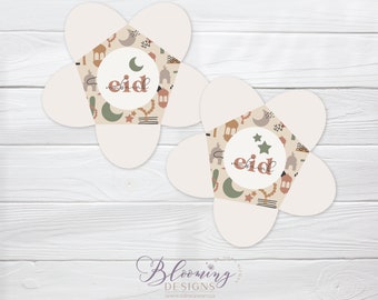 May include: Two white paper flower boxes with a beige background and a pattern of stars, crescent moons, lanterns, and mosques. The center of each box has a white circle with the word "eid" in brown text.
