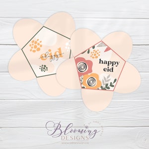 May include: Two pink flower-shaped paper boxes with a hexagonal window. The boxes have a floral pattern and the text "happy eid" inside the window.