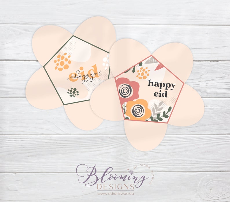 May include: Two pink flower-shaped paper boxes with a hexagonal window. The boxes have a floral pattern and the text "happy eid" inside the window.