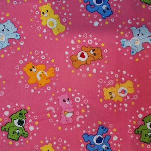May include: Pink fabric with a repeating pattern of Care Bears. The bears are in various colors and poses, including blue, orange, green, pink, and brown. The background is pink with white stars and hearts.