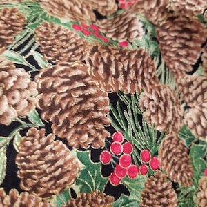 May include: A black fabric with a repeating pattern of brown pine cones and red berries. The pine cones have a gold metallic sheen.