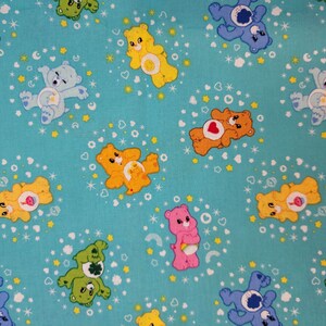 May include: A turquoise fabric with a repeating pattern of Care Bears. The bears are in various colors and poses, including a blue bear with a star, a yellow bear with a heart, a pink bear with a rainbow, and a green bear with a clover. The background is a light blue with white stars.