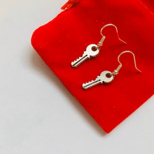 Puede incluir: Un par de pendientes de plata en forma de llave sobre una bolsa de terciopelo rojo.