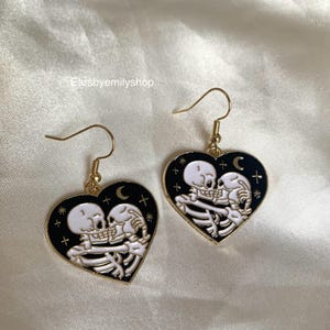 クールで風変わりな黒いハートとキスする白いスケルトンのドロップダングルのハロウィンイヤリング。18K ゴールドメッキのフック付き。