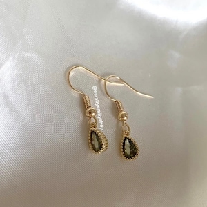 May include: A pair of gold teardrop earrings with green gemstone accents. The earrings have a delicate, feminine design.