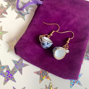 Peut inclure: Une paire de boucles d'oreilles en or avec un motif de tasse à thé en porcelaine bleue et blanche. Les boucles d'oreilles sont présentées sur une pochette en velours violet.