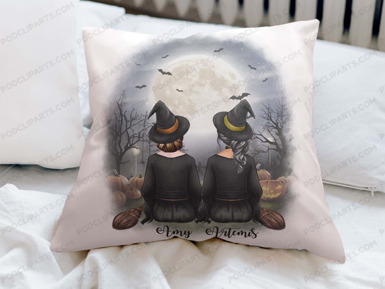 May include: A white pillow with a Halloween-themed design featuring two witches with black hats and broomsticks. The witches are standing in front of a full moon and pumpkins. The text "Amy Artemis" is printed below the witches.