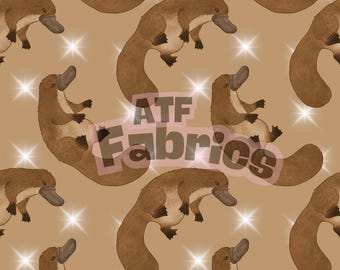 May include: A repeating pattern of cartoon platypuses in shades of brown and tan, with a light brown background and sparkling starbursts. The text "ATF Fabrics" is overlaid on the image.