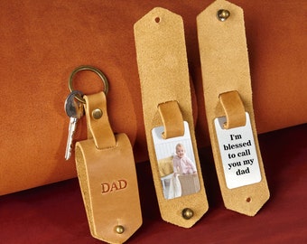 May include: Two leather keychains with metal rings. One keychain has the word "DAD" engraved on it. The other keychain has a photo of a child and the text "I'm blessed to call you my dad".
