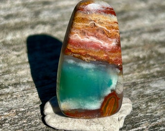 Puede incluir: Una piedra de ágata pulida, lisa, de color verde, marrón y blanco con forma de lágrima.