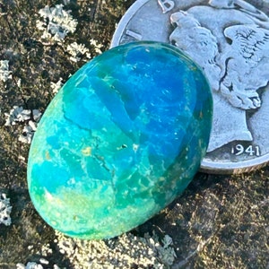 May include: A bright blue and green cabochon gemstone with a marbled pattern. The gemstone is oval-shaped and is about the size of a US half dollar coin.