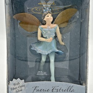 May include: A Hallmark Faerie Estrella figurine in a clear plastic box. The fairy is wearing a light blue dress and has brown and gold wings. The box reads "Faerie Estrella" and "Frostlight Faeries Collection".